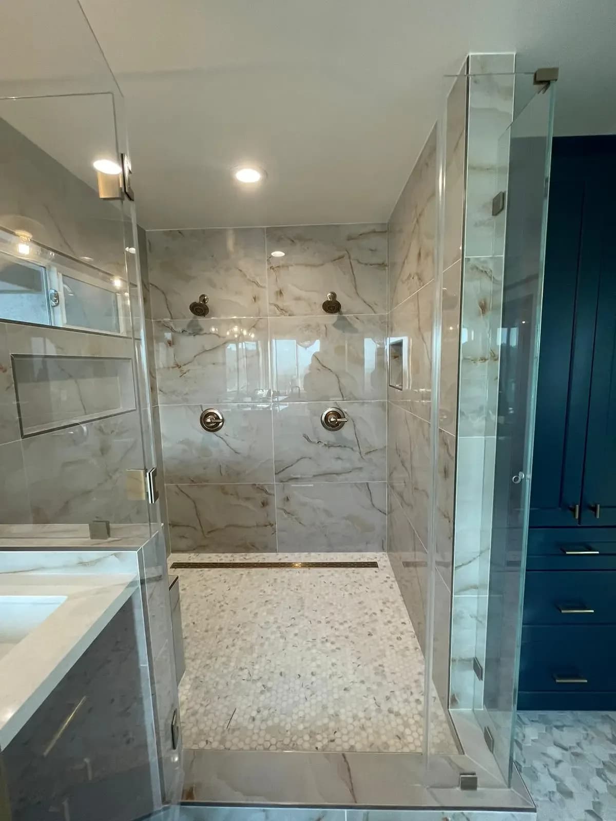 Walk-in shower with marble-look walls, pebble floor and a rain head