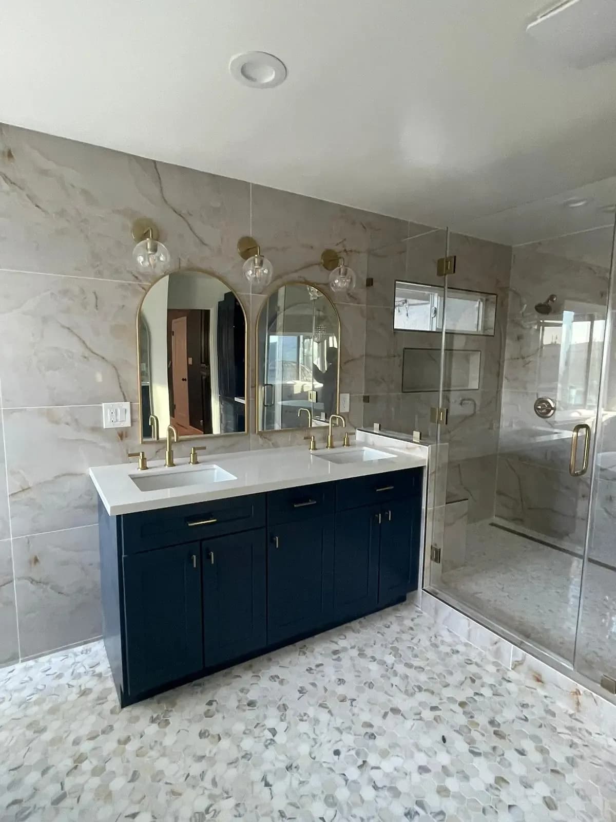Bathroom with a navy vanity, arched mirrors and marble-pattern tile