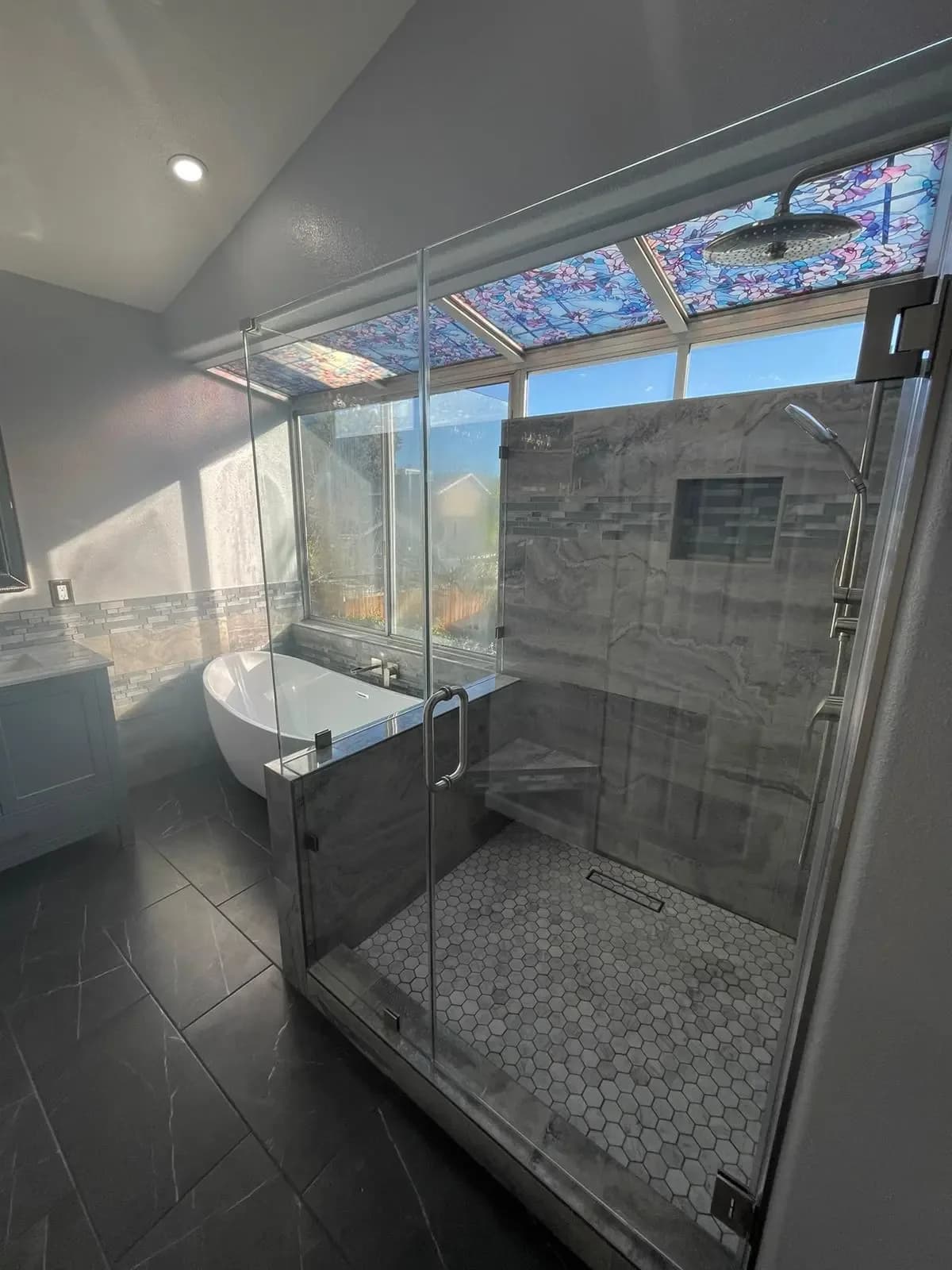 Frameless glass shower beside a freestanding tub under a skylight